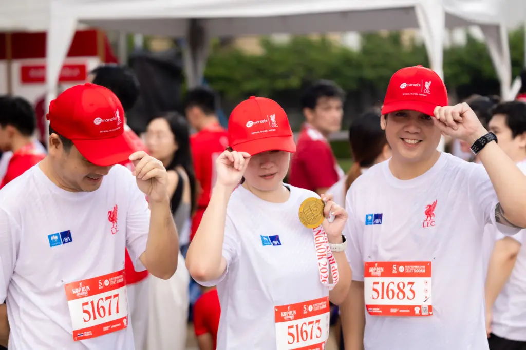 Group of runners in white shirts and red caps at a race, smiling and adjusting their hats, bib numbers visible: 51677, 51683, 51673, etc.